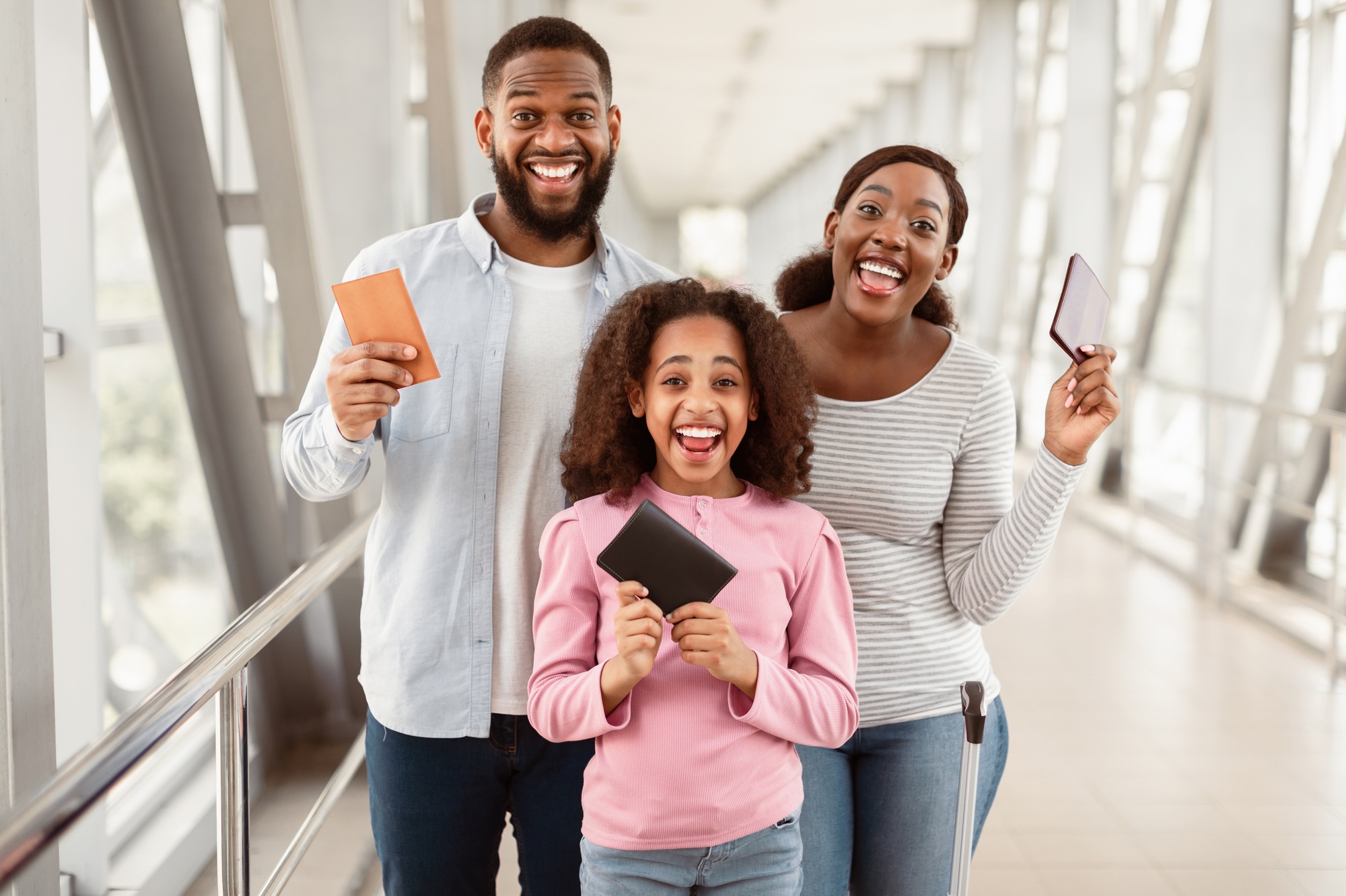 Happy excited black family traveling, holding documents in airport
